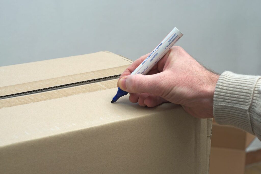 A person uses a black permanent marker to label a cardboard box for storage.